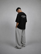 Person wearing a black t-shirt with a logo on the back, standing against a gray background