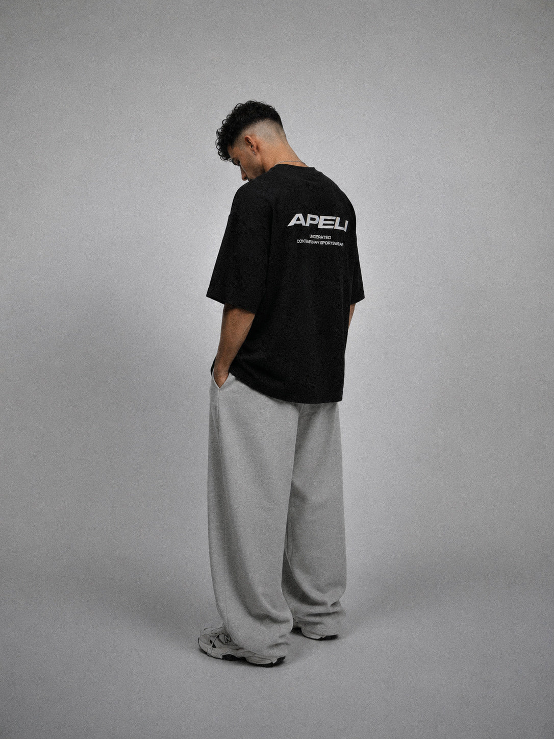 Person wearing a black t-shirt with a logo on the back, standing against a gray background