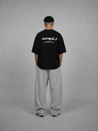 Person wearing a black t-shirt with 'APELI' logo on the back, standing against a gray background