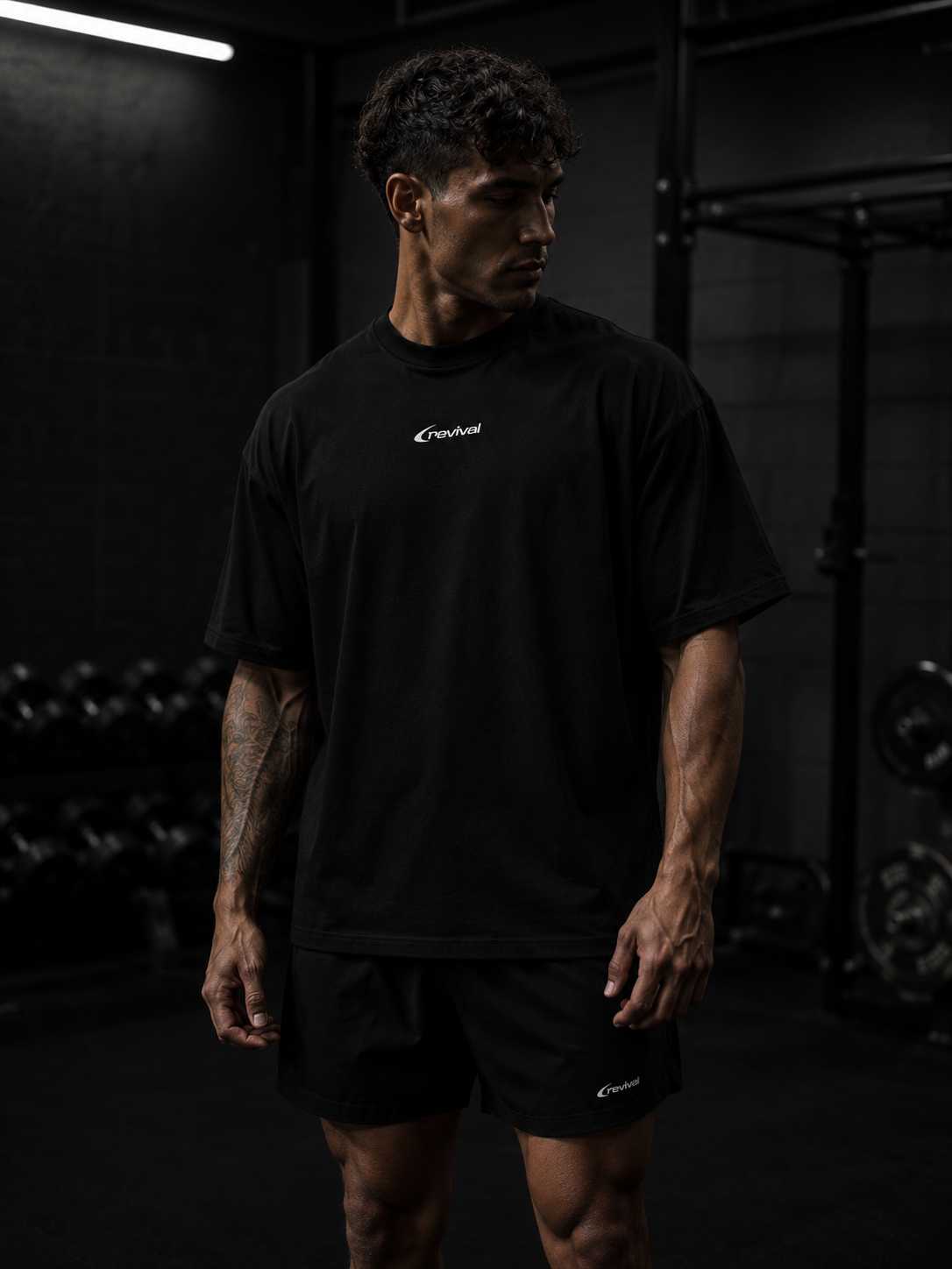 A man in a black athletic t-shirt and matching shorts stands in a dark gym environment. The brand name 'CruzeFit' is printed in white on the chest of the t-shirt.