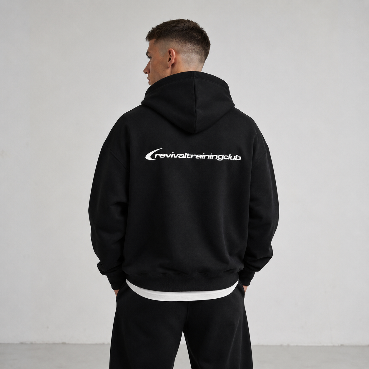 Person wearing a black hoodie with 'revivaltrainingclub' logo on the back against a plain background